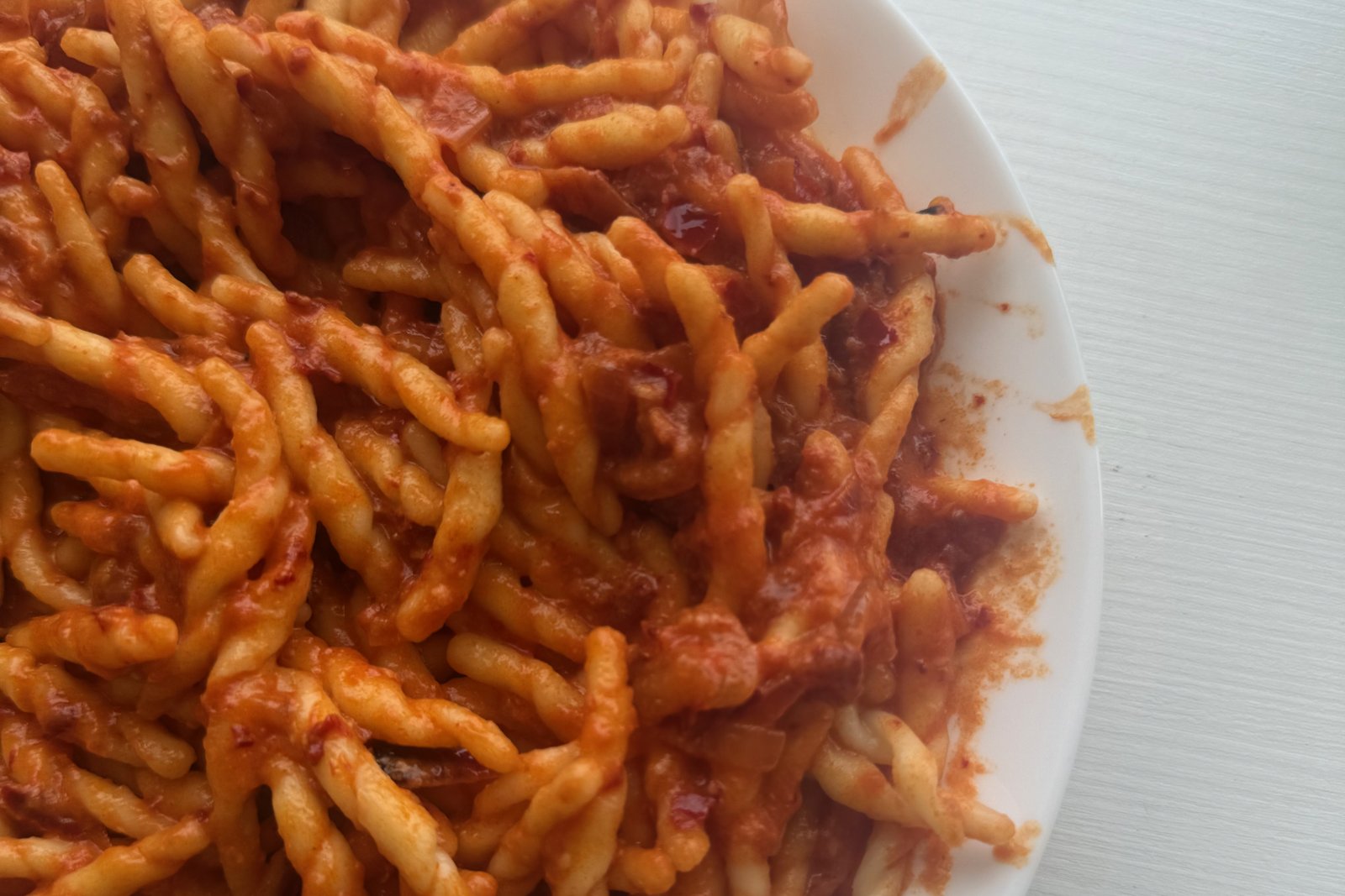 Talerz skręconego makaronu trofie w czerwonym sosie z ndują i cebulą