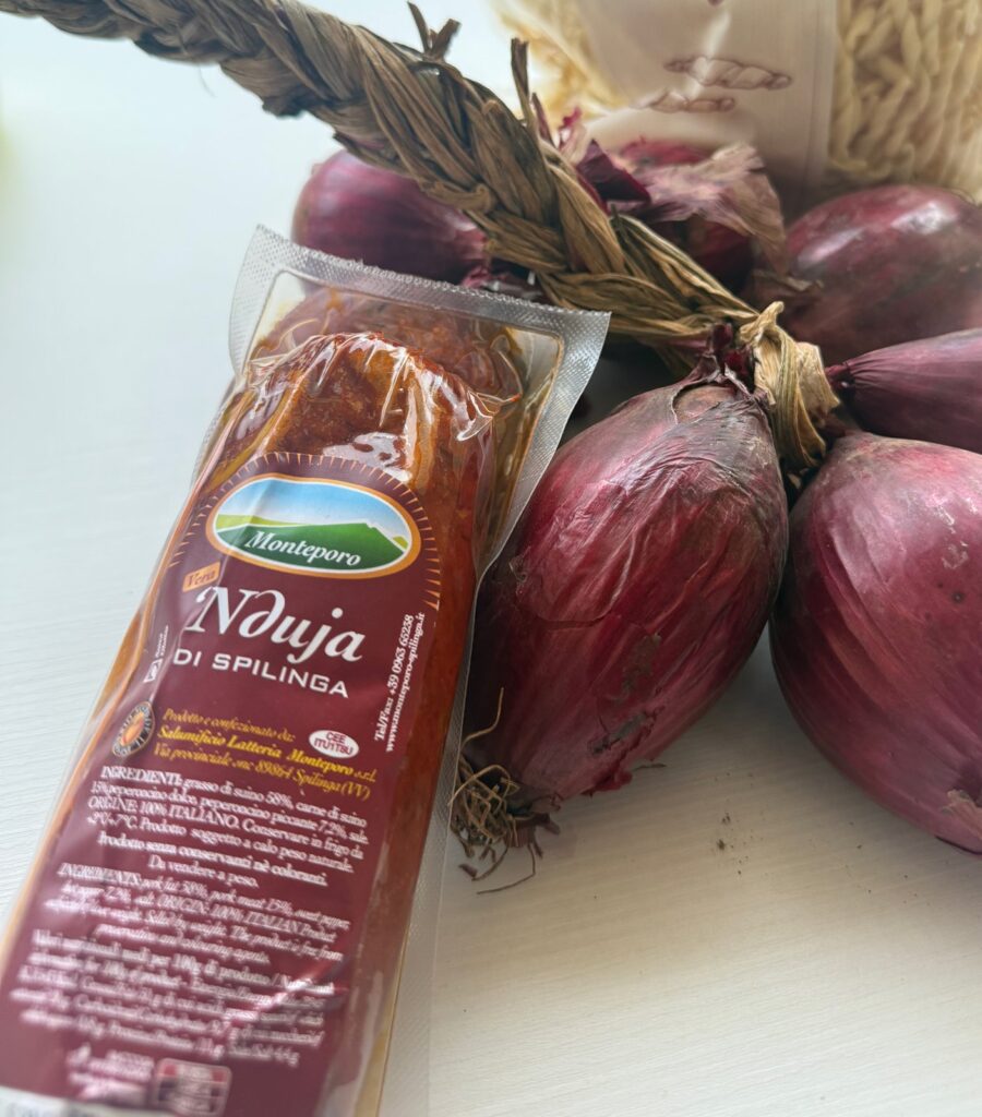 'Nduja di Spilinga w osłonce i opakowaniu próżniowym obok cebul z Tropei, widoczna etykieta ze składem