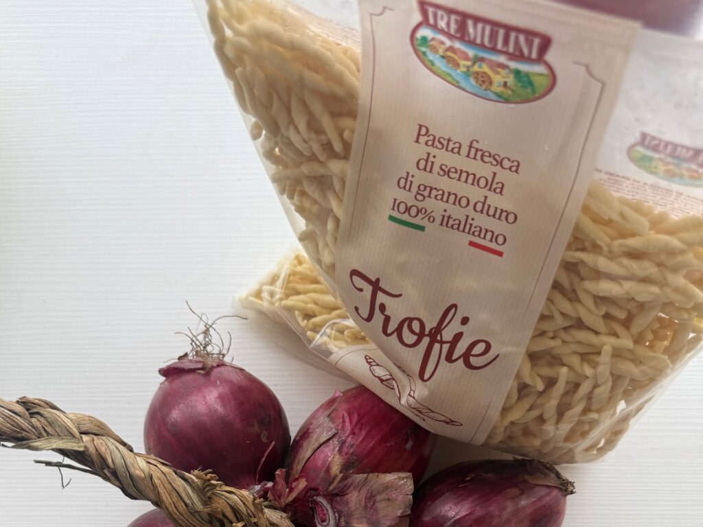 Paczka świeżego makaronu trofie z semoliny obok czerwonych cebul
