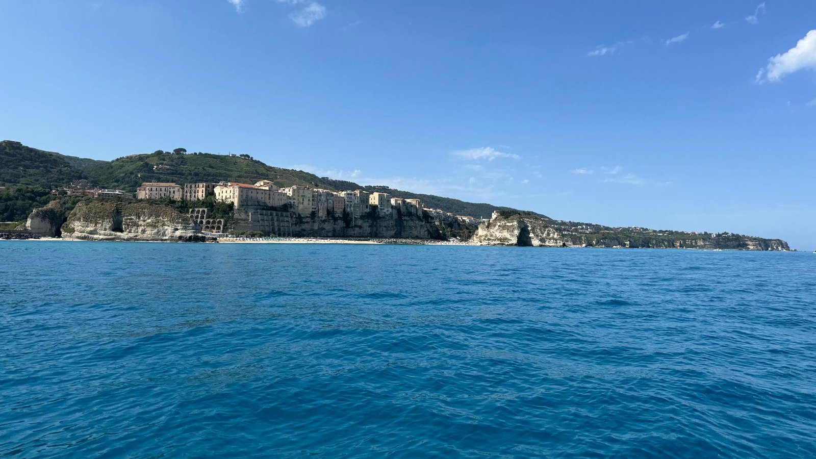 Tropea widziana z łodzi: domy starego miasta na klifie nad plażą i skała Santa Maria dell'Isola